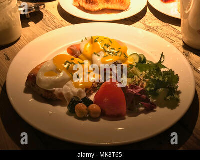 Uova Benedict con salmone affumicato su fette di pane abbrustolito servito con olio d'oliva, pomodori e insalata fresca per colazione. Foto Stock