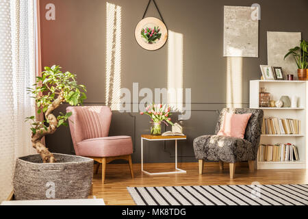 Albero di Bonsai in elegante salone interno con fiori su tavola tra rosa e grigio poltrona Foto Stock