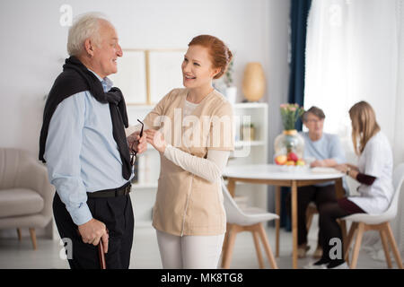 Offerta attenzione del personale medico verso anziani uomo e donna, parlando, spiegando, conforto in lussuosa struttura di cura sala comune Foto Stock