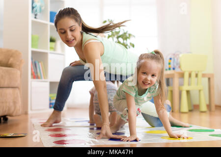 Giovane madre twister giocando con i suoi bambini. Allegro la famiglia a casa. La famiglia felice giocare insieme Foto Stock