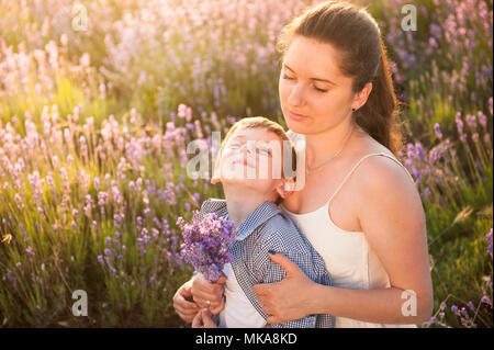 La famiglia felice composta da madre e bambino sogna seduta compresi tra estate campo di fiori Foto Stock
