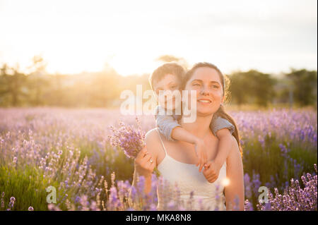La famiglia felice costituito da madre bella e vivace sognando il bambino seduto compresi tra estate campo di fiori Foto Stock