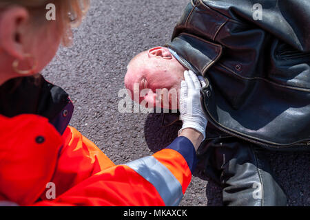 Un tedesco paramedico controllare la pressione del sangue su un ferito biker Foto Stock