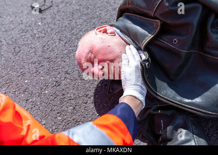 Un tedesco paramedico controllare la pressione del sangue su un ferito biker Foto Stock