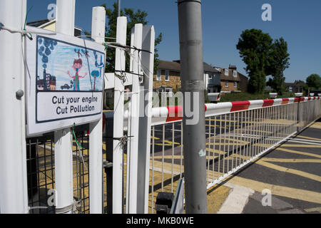 Tagliare il vostro motore di taglio segno di inquinamento con il bambino del disegno in corrispondenza di un passaggio a livello ferroviario in East Sheen, Londra, Inghilterra Foto Stock