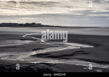 Un flusso si snoda attraverso velme a bassa marea a Morecambe Bay, con il lungomare di Sandylands e Heysham Power Station in background. Foto Stock