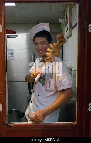 Cuoco cinese a lavorare nel ristorante asiatico cucina a Pechino in Cina, Asia. Tradizionale negozio di alimentari nel mercato locale. Chef calamari vendita su spiedini Foto Stock