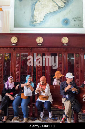 Le donne musulmane di indossare il velo islamico seduta su una panchina di fronte di cabine telefoniche in l'Ufficio postale centrale, la città di Ho Chi Minh, Vietnam. Foto Stock