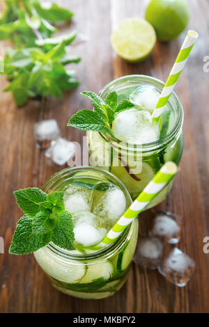 Due vasi di frutta e infusi di erbe di acqua con il cetriolo, calce, menta e pezzi di ghiaccio su un tavolo di legno. Il concetto di disintossicazione e perdita di peso. Foto Stock