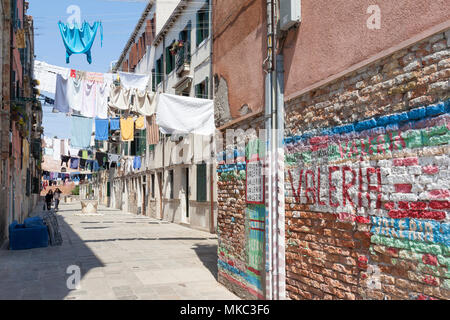 Washday nel Castello, Venezia, Veneto, Italia con una vista passato colorato di graffiti su un weathered muro di mattoni di vestiti appesi sulle linee in un campiello wi Foto Stock