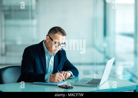 Inquadratura di un senior financial imprenditore seduto alla sua postazione di lavoro nella parte anteriore del computer e laptop mentre facendo alcune pratiche. Foto Stock