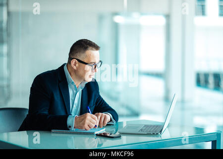 Inquadratura di un senior financial imprenditore seduto alla sua postazione di lavoro nella parte anteriore del computer e laptop mentre facendo alcune pratiche. Foto Stock