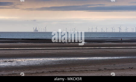 Liverpool, in Inghilterra, Regno Unito - 12 Novembre 2016: il sole tramonta dietro di Antony Gormley "UN ALTRO POSTO' sculture su Crosby Beach, e fattorie eoliche e il fare Foto Stock