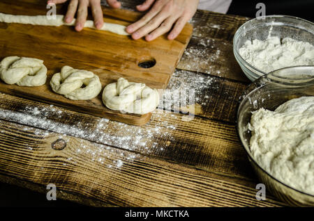 Impasto ormeggiata sulla tavola di legno, tradizionale pretzel preparazione, baker rendendo la pasta di pane nel forno. mani giocate con farina e pasta. Foto Stock