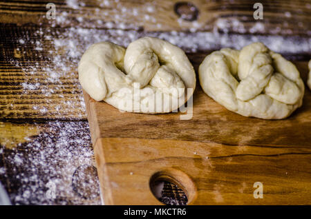 Impasto ormeggiata sulla tavola di legno, tradizionale pretzel preparazione, baker rendendo la pasta di pane nel forno. mani giocate con farina e pasta. Foto Stock