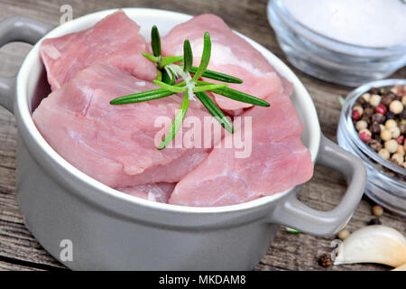 Pezzi di carne di maiale in una pentola con le spezie su una tavola di legno Foto Stock