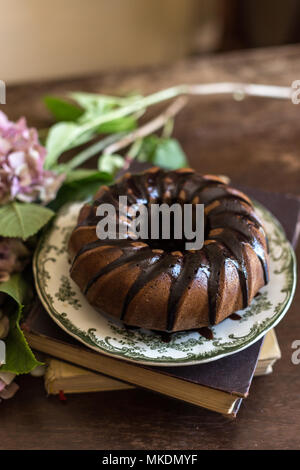 Deliziosa torta al cioccolato nella splendida annata piastra ceramica sul piano portapaziente rustico con fiori di colore rosa. Composizione verticale. Foto Stock