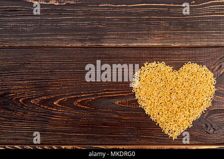 Maccheroni stelline cuore, vista dall'alto. Cuore dal cibo crudo su sfondo di legno, copia dello spazio. Il giorno di San Valentino la decorazione. Foto Stock