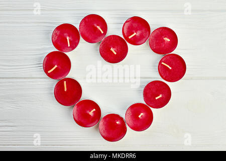 Forma di cuore da tè rosso accendono le candele. Candele rosse formando la forma del cuore sulla luce sullo sfondo di legno, vista dall'alto. Amore e romanticismo concetto. Foto Stock