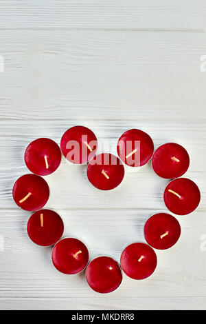 Cuore rosso da candele e copia dello spazio. Tè rosso luce di candele profumate formando forma di cuore in bianco sullo sfondo di legno, vista dall'alto. Il giorno di San Valentino saluto Foto Stock