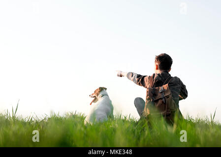 Adolescente sul prato verde con un piccolo cane bianco Foto Stock