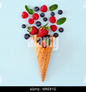 Un assortimento di frutti di bosco in cialda cono gelato. Piatto concetto laici su un pastello blu sullo sfondo. Foto Stock