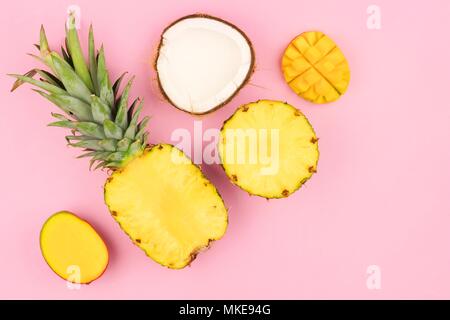 Frutta tropicale laici piatto con ananas e mango, e noce di cocco su un pastello sfondo rosa. Angolo di orientamento. Foto Stock