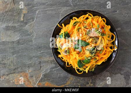 La zucca spirilized tagliatelle con spinaci e semi di zucca su ardesia scura sullo sfondo, mangiare sano concetto. Vista dall'alto. Foto Stock