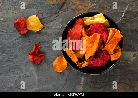 Ciotola di miste di ortaggi sani chip. Vista dall'alto, ancora in vita su una pietra scura sullo sfondo. Foto Stock