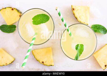 Due bicchieri di succo di ananas con le foglie di menta. Vista dall'alto su un marmo bianco dello sfondo. Foto Stock