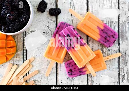 Gruppo di fatti in casa mango popsicles blackberry, vista dall'alto su un rustico di legno bianco sullo sfondo Foto Stock