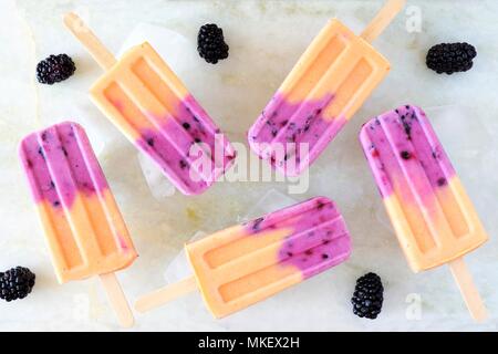 Gruppo di mango yogurt blackberry popsicles con ghiaccio. Vista dall'alto su un marmo bianco dello sfondo. Foto Stock