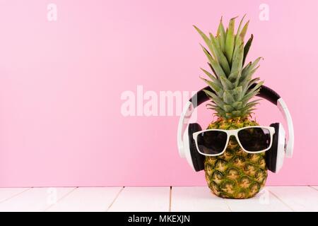 Hipster ananas con occhiali da sole e le cuffie contro un sfondo rosa. La minima nozione d'estate. Foto Stock