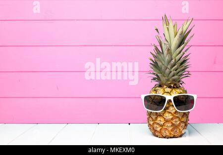 Hipster ananas con occhiali da sole contro una rosa di sfondo di legno Foto Stock