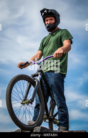 Allegro sportivo estremo nel casco in piedi sulla moto e guardando la fotocamera Foto Stock