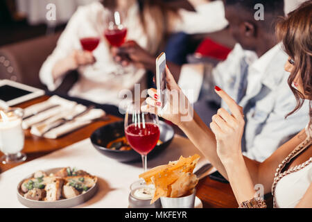 Close up dei womans mani con perfetta manicure rosso tenendo selfie presso il ristorante Foto Stock