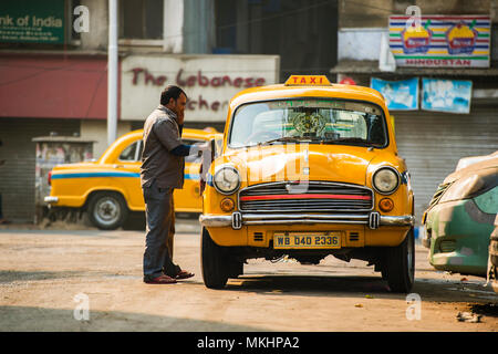 KOLKATA - INDIA - 21 GEN 2018: un ambasciatore della cabina unità di taxi ha il lavaggio del suo vecchio taxi giallo al tramonto. Foto Stock