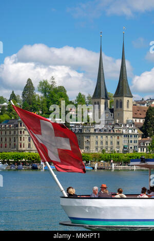 La barca con bandiera svizzera naviga sul lago di Lucerna di fronte alla Chiesa di San Leodegar, Lucerna, Svizzera, Europa Foto Stock