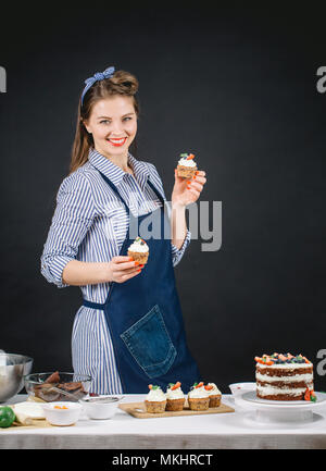 Attraente donna europea tenendo i tortini in mani dando culinary master class in studio Foto Stock