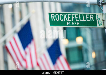 Vista ravvicinata di green street segno raffigurante è Rockefeller Plaza in Midtown Manhattan, New York. Sfocato bandierine americane in background Foto Stock