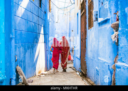 Due donne abbigliate con vestiti tradizionali Saree Indiani stanno passeggiando per le stradine della città blu di Jodhpur, Rajasthan, India. Foto Stock