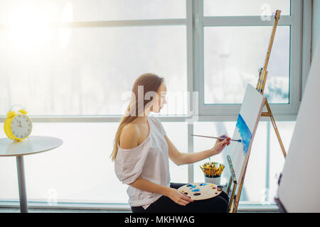 Con i capelli lunghi pittore dilettante donna prendendo lezioni di disegno seduta in arte-scuola camera inondata di luce solare Foto Stock