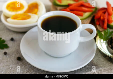 Una tazza di caffè forte (espresso), close-up e facile dieta colazione - uova sode e pane marrone con verdure fresche (cetriolo, paprika). Foto Stock