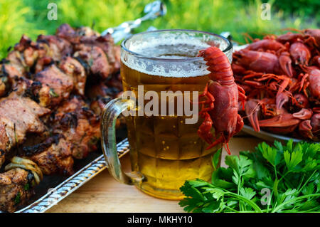 Schiumoso la birra in un bicchiere e aragosta bollita, grigliate di carne su spiedini in background. Per le vacanze, godendo la vita all'aperto. Foto Stock