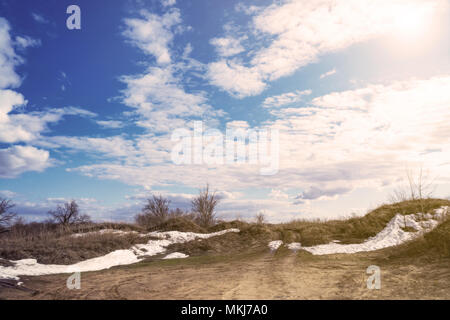 La sabbia grigia, un cielo nuvoloso e l'ultima neve alla luce del sole Foto Stock