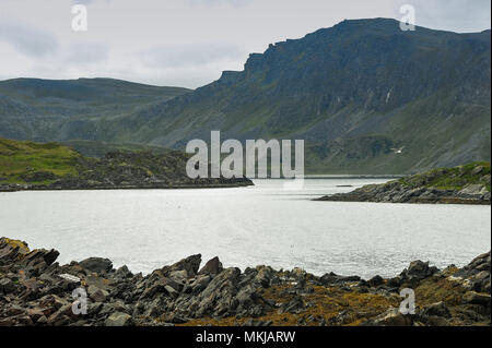 Bellissimo paesaggio nordico, Isola Mageroya, Nordkapp, Norvegia. Montagne scoscese, fiordo di calma e di ingresso di un roccioso in primo piano. Foto Stock