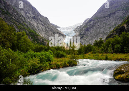 Il Ghiacciaio Briksdal il timone e il fiume, in Jostedalsbreen National Park, Norvegia (lunga esposizione). Lussureggiante foresta verde, aqua acqua e cielo grigio panorama Foto Stock