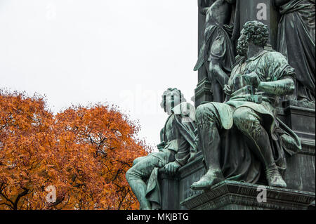 Golden Autumn Leaves ben giustapposto contro due figure che rappresentano la gioventù e l'età adulta, su Friedrich Schiller statua a Vienna, in Austria Foto Stock