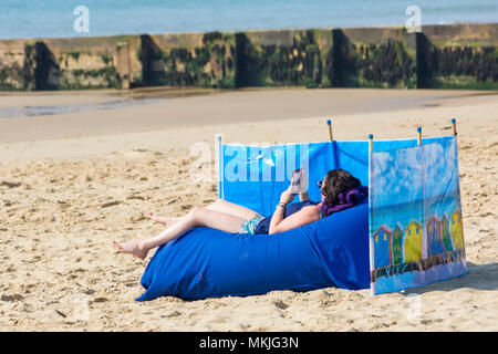 Bournemouth Dorset, Regno Unito. 8 maggio 2018. Regno Unito: meteo sole caldo per iniziare la giornata, come una giovane donna si rilassa sulla spiaggia ad Alum Chine beach leggendo il suo kindle. Credito: Carolyn Jenkins/Alamy Live News Foto Stock