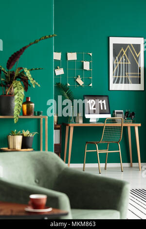 Golden Sedia in metallo e un moderno home office con computer in un angolo di un elegante salotto interno con piante e pareti di colore verde Foto Stock